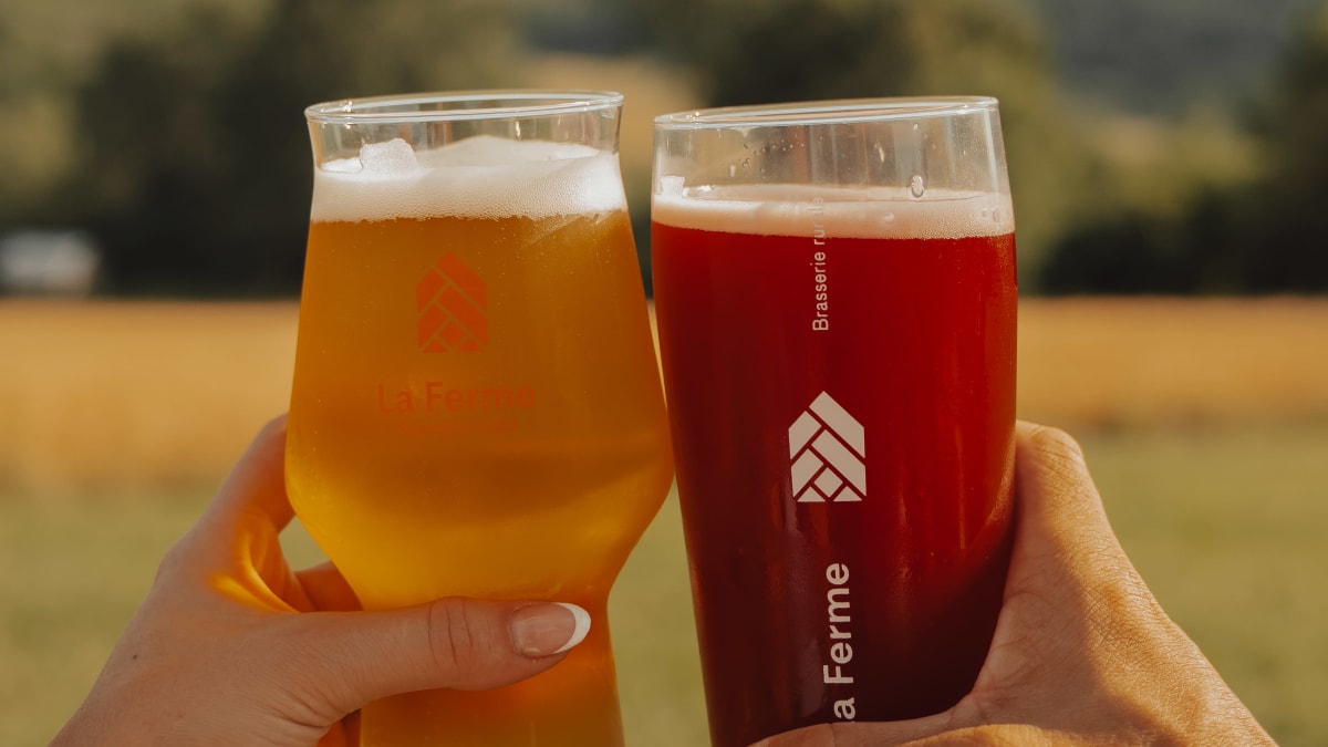 Two glasses of beer held by people outside the frame in front of a mountainous landscape.