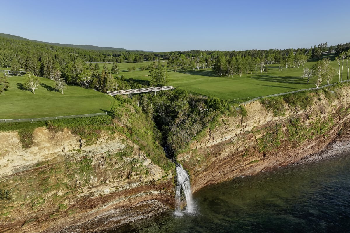 Aux limites d'un terrain de golf verdoyant, un plan d'eau rencontre une falaise rougeâtre. 