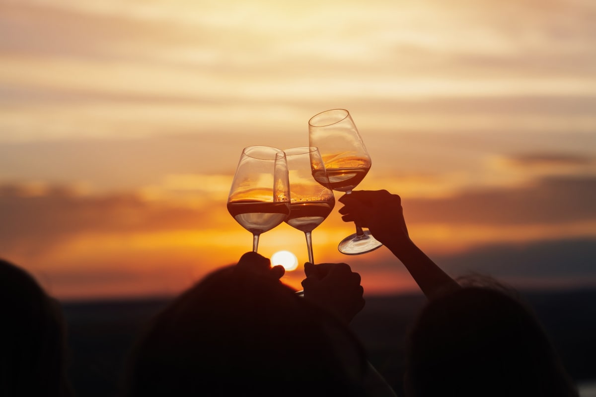 Trois verres de vin levés devant un coucher de soleil