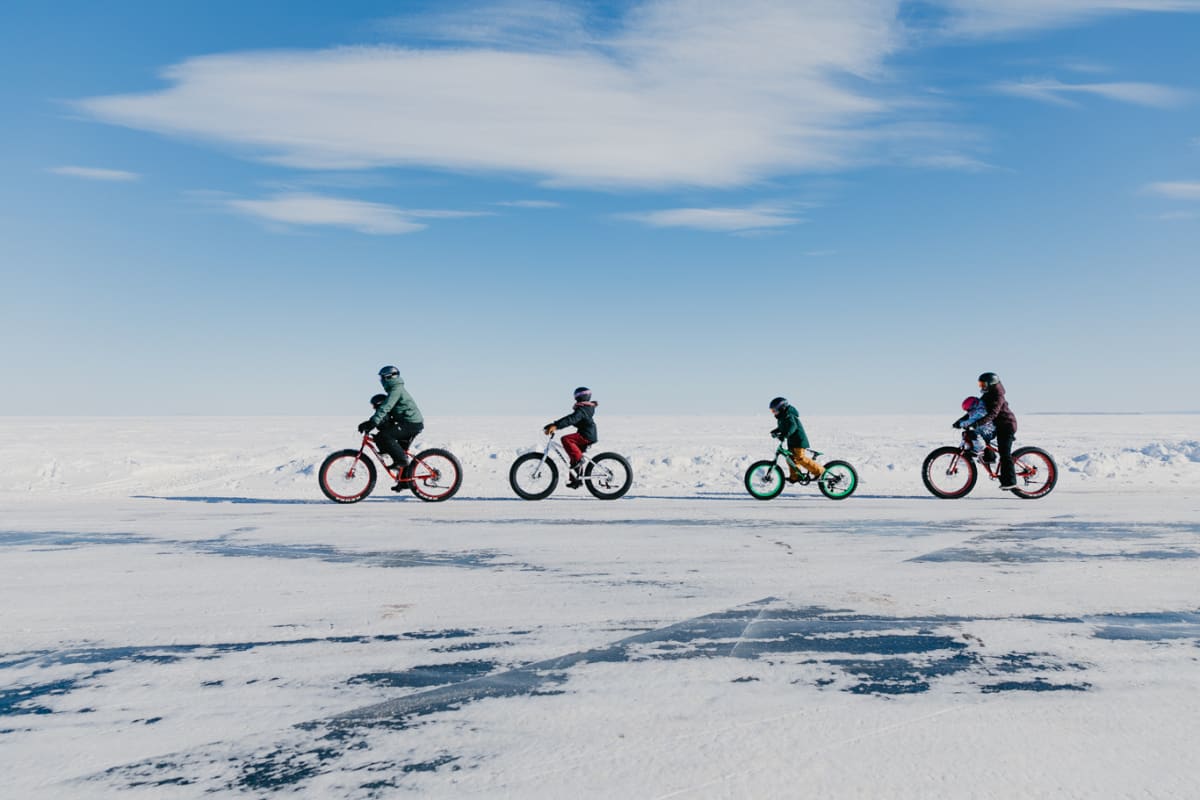 Four people on bicycles, riding one behind the other in a snowy landscape.
