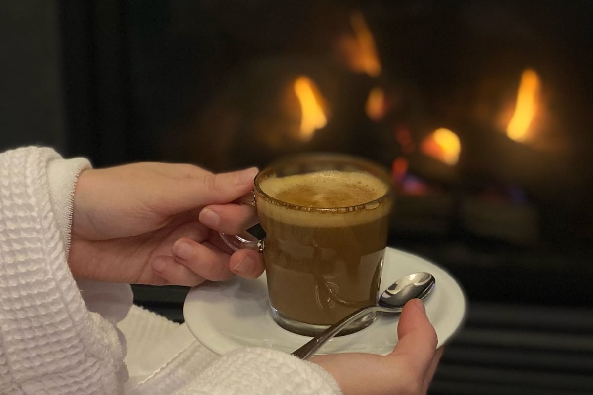 Femme en peignoir avec un café dans les mains devant un foyer.