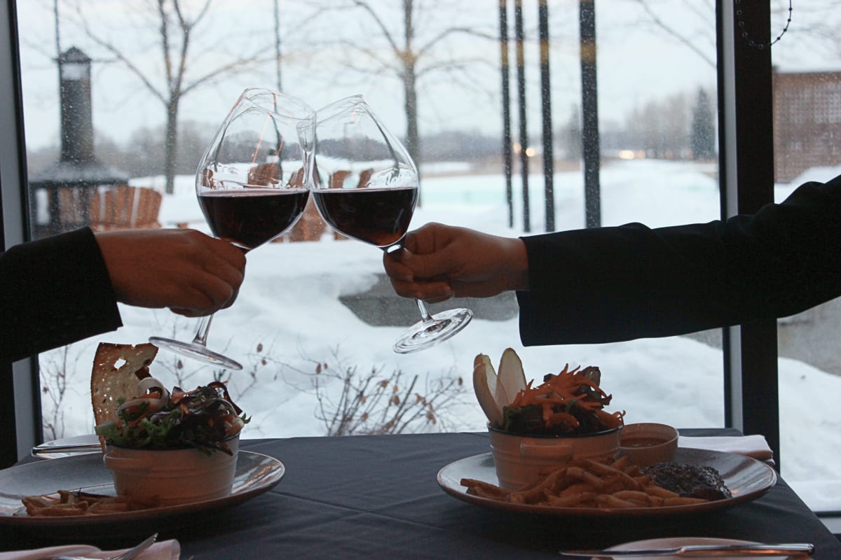 Deux personnes qui trinquent devant la fenêtre d'un resto en hiver.