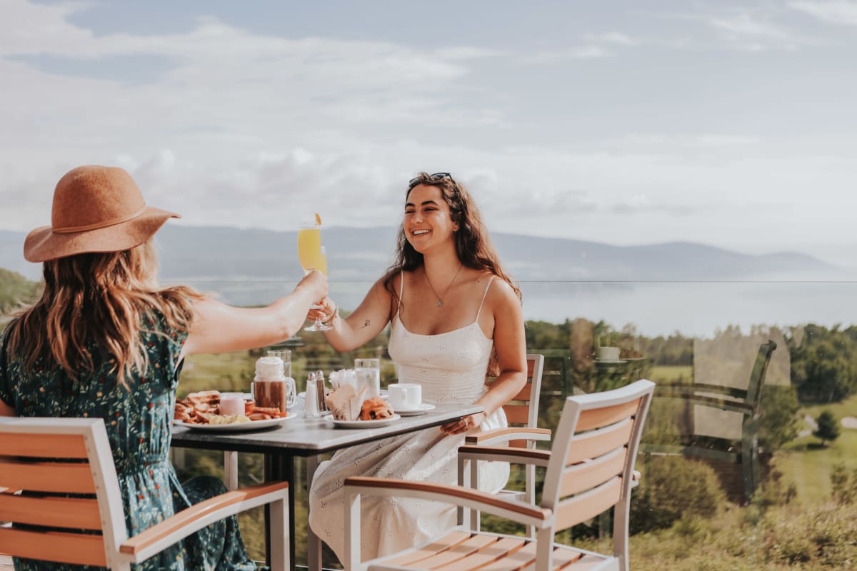 Deux femmes sur une terrasse ensoleillée en train de trinquer.