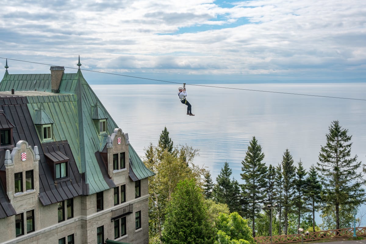 Personne en tyrolienne au dessus du Fairmont Le Manoir Richelieu, avec le fleuve en arrière-plan.