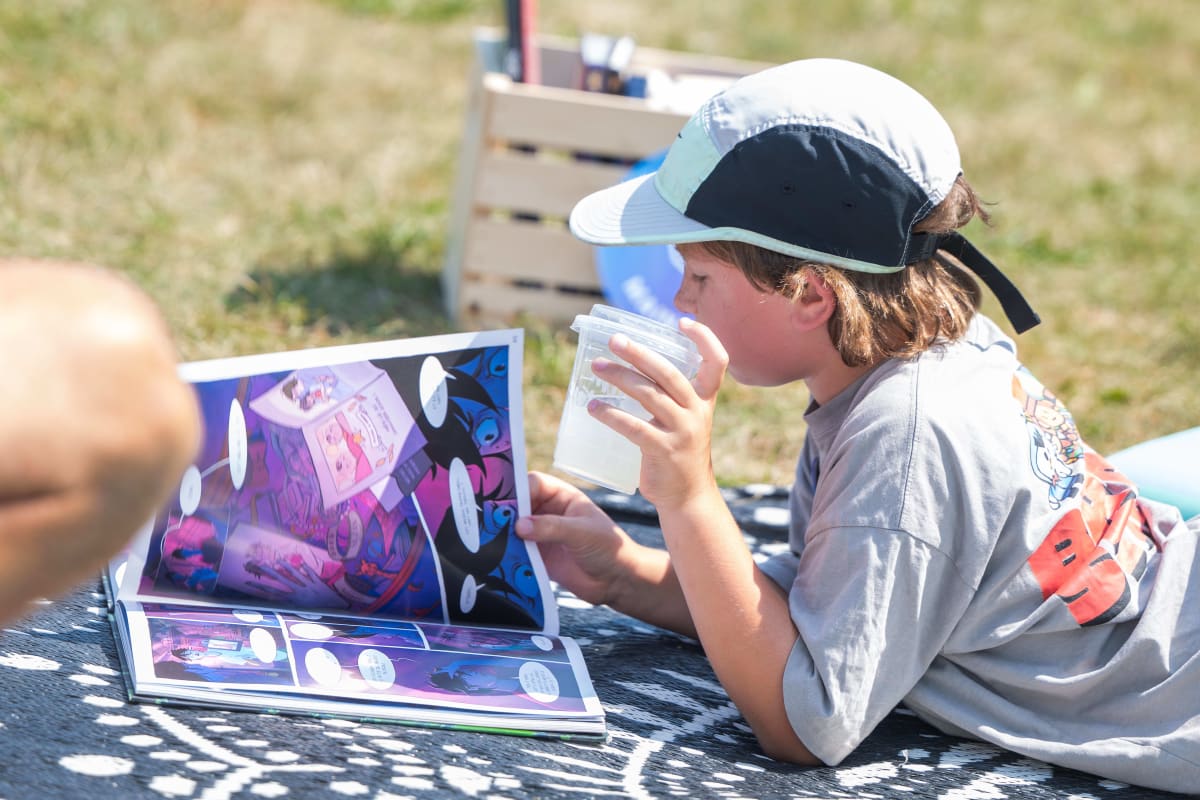 A boy lying on a blanket, reading a comic book
