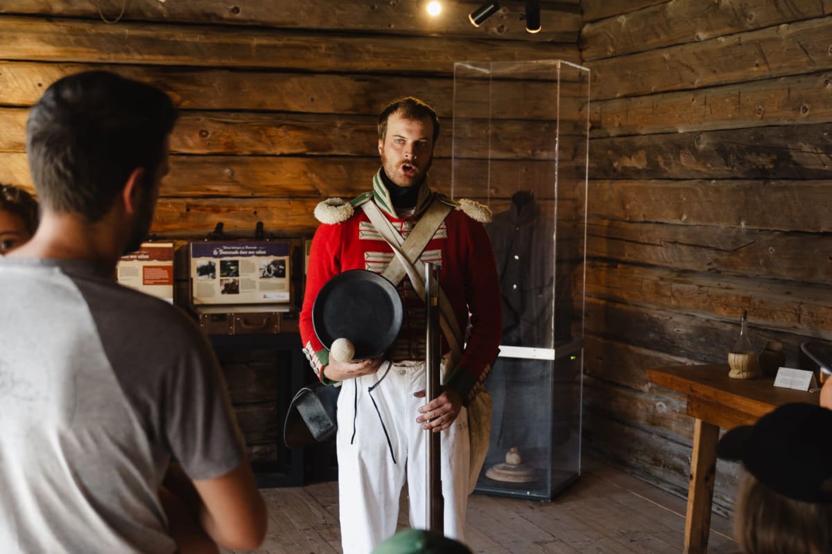 Soldat en uniforme qui se tient devant une famille dans un ancien bâtiment en bois.