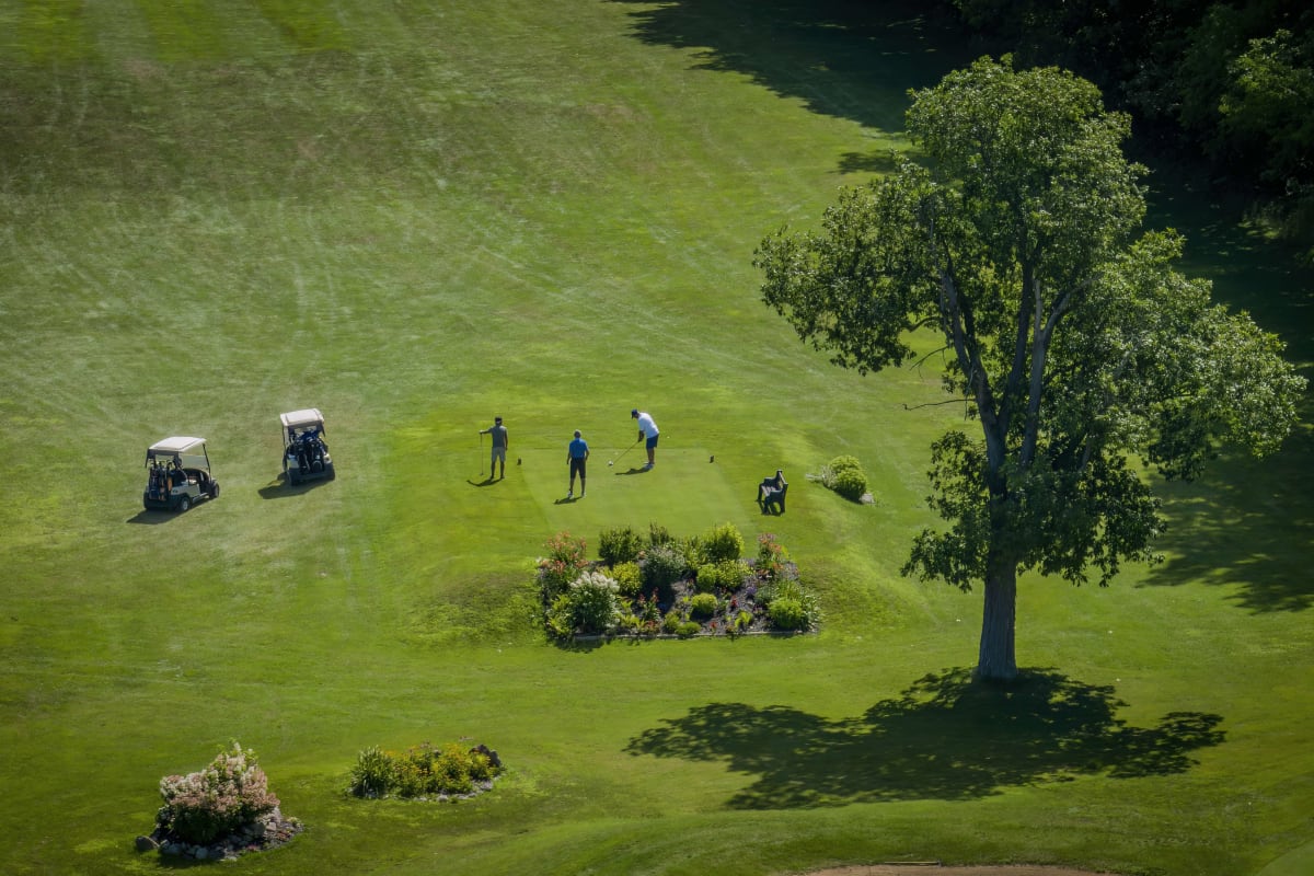 Trois golfeurs et deux voiturettes vus de haut sur un tertre de départ à La Cache du Lac Champlain.