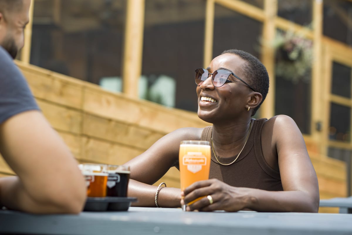 Femme assise à une table extérieure en train de prendre une bière à la Microbrasserie Kahnawake.