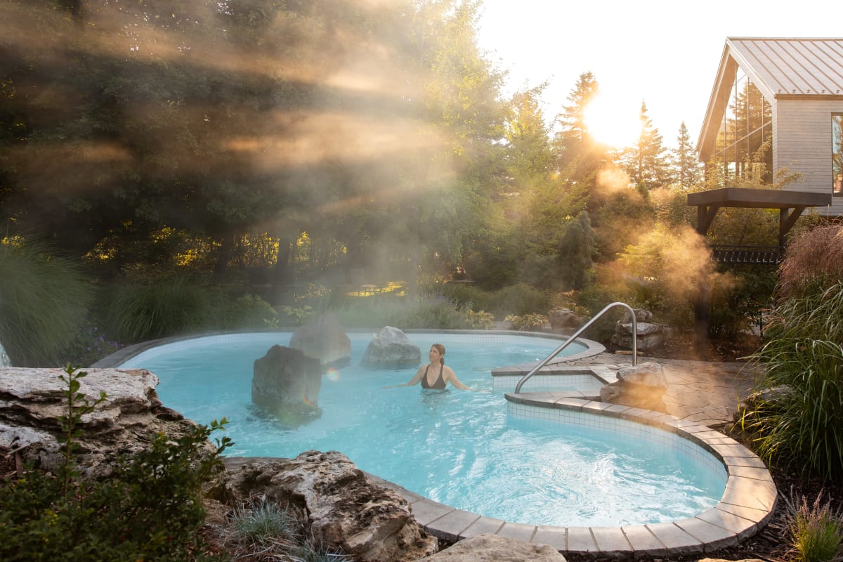 Femme dans un bain thermal au Strom spa nordique Mont-Saint-Hilaire; la scène est baignée d'une lumière dorée.