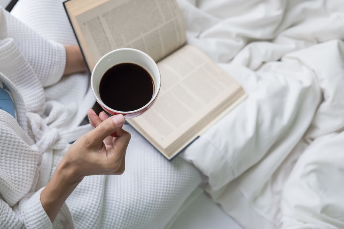 Femme couchée dans un lit avec une tasse de café.