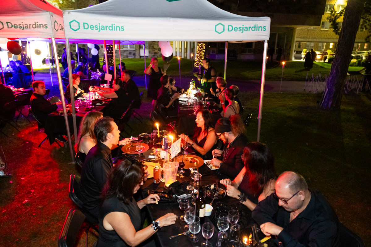 Groups of people dressed in black, seated at a long outdoor table