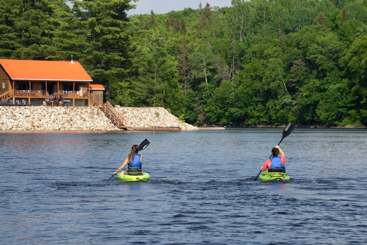 Deux personnes en kayak sur le lac devant un chalet.