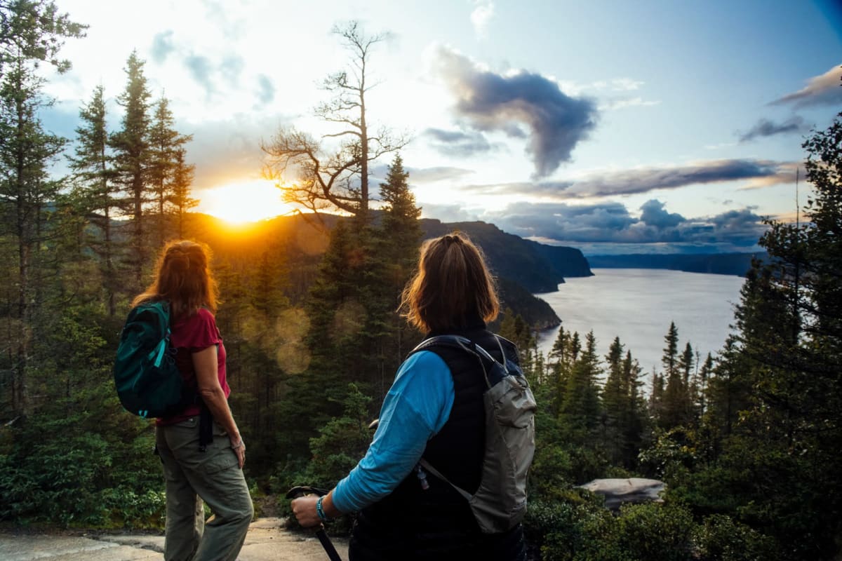 Parc national du Fjord-du-Saguenay - Deux femmes en haut d'une montagne, la forêt et le couché de soleil en arrière-plan.