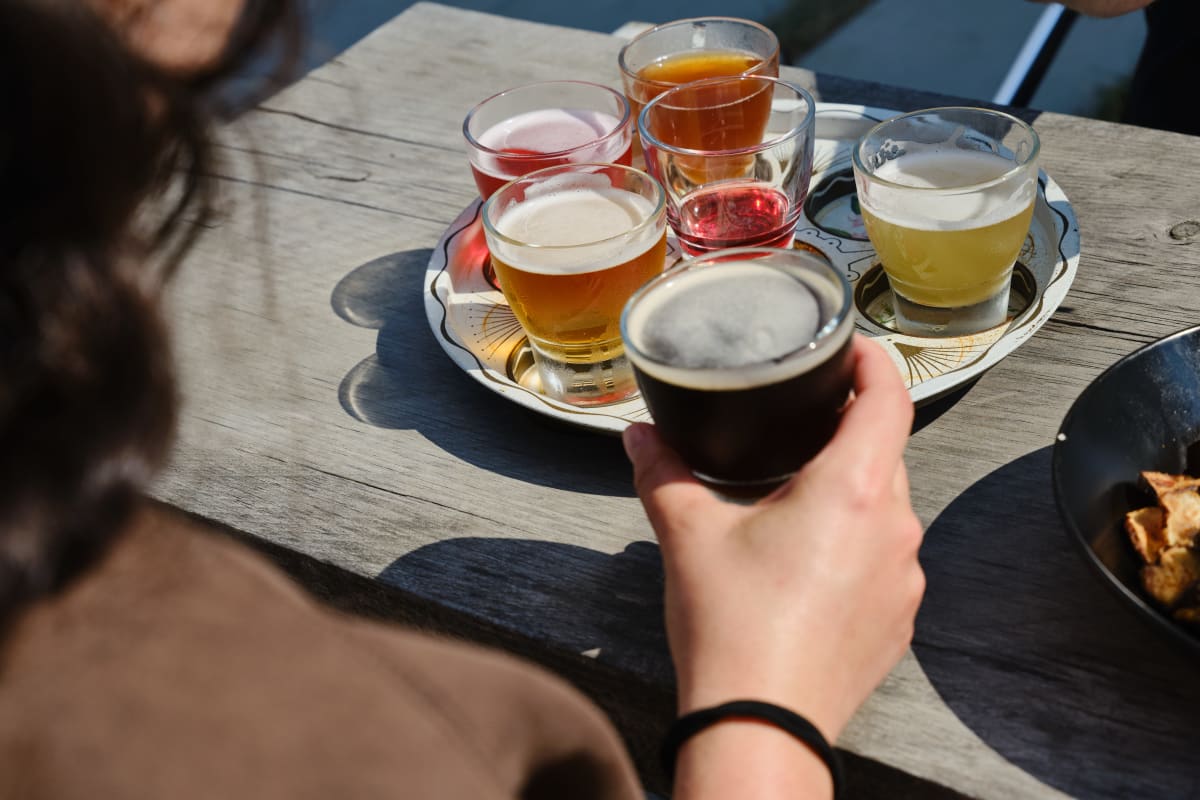 Plateau de dégustation de bières; à l'avant-plan, une personne tient un verre bien rempli.