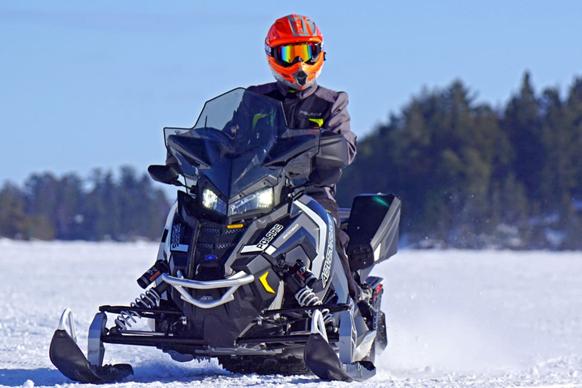 Motoneigiste sur sa motoneige sur la neige avec la forêt derrière.