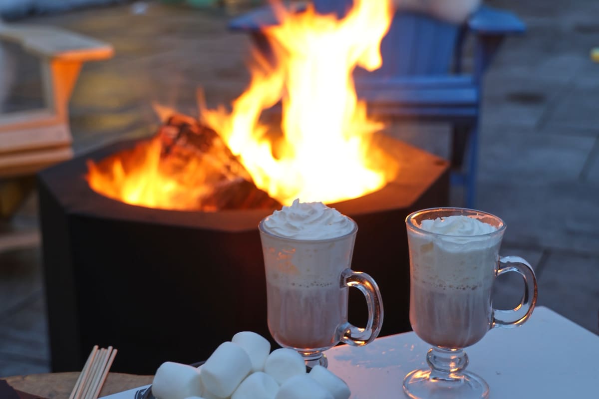 Feu extérieur avec des tasses de chocolat chaud et les ingrédients pour faire des s'mores.