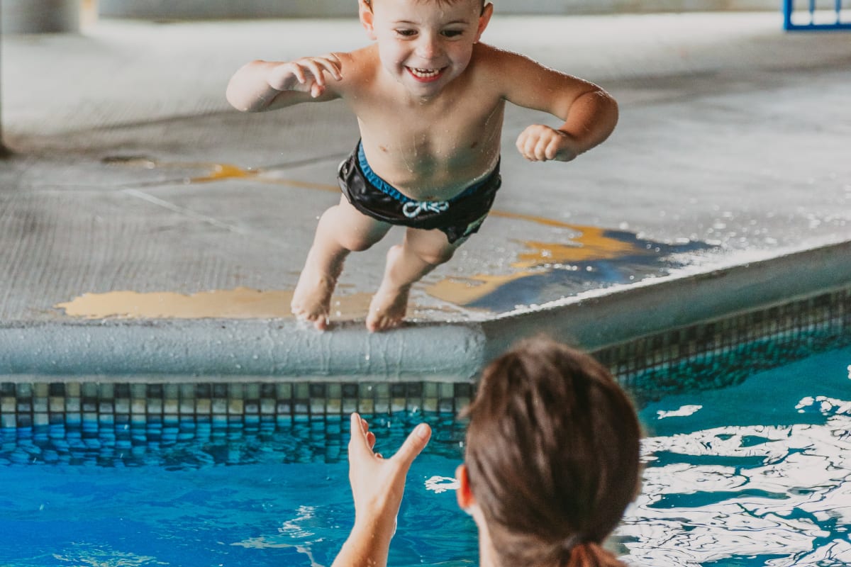 Mère dans la piscine d'hôtel qui attrape son fils qui saute dans l'eau.