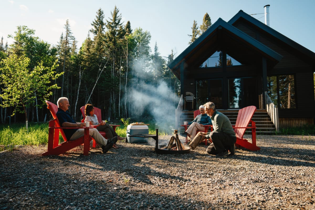 Four people sitting in Adirondack chairs around a field fire in front of a Horizon cabin.