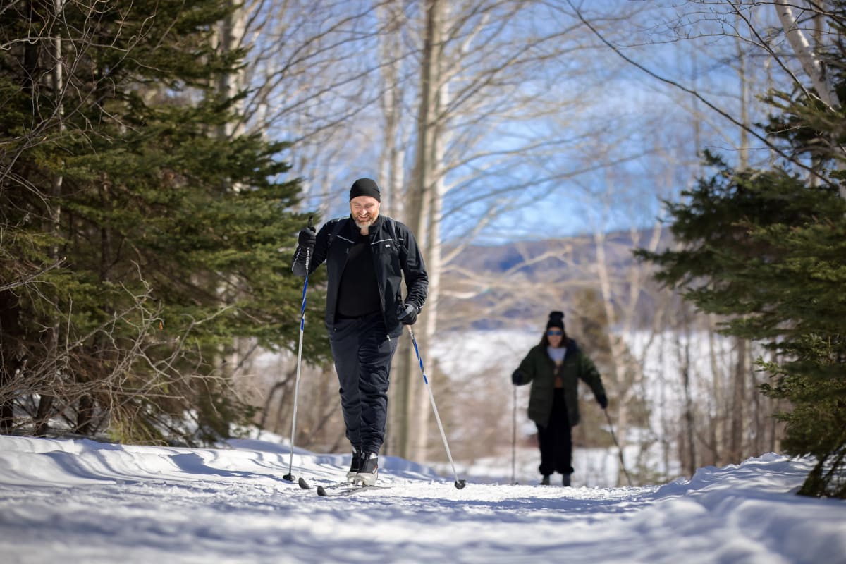 Deux personnes en ski de fond dans une forêt par un temps ensoleillé.