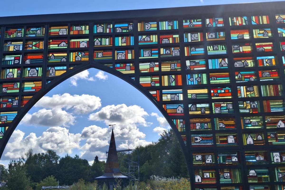 Installation artistique extérieure de plusieurs images en vitraux assemblées pour former un paysage rural.