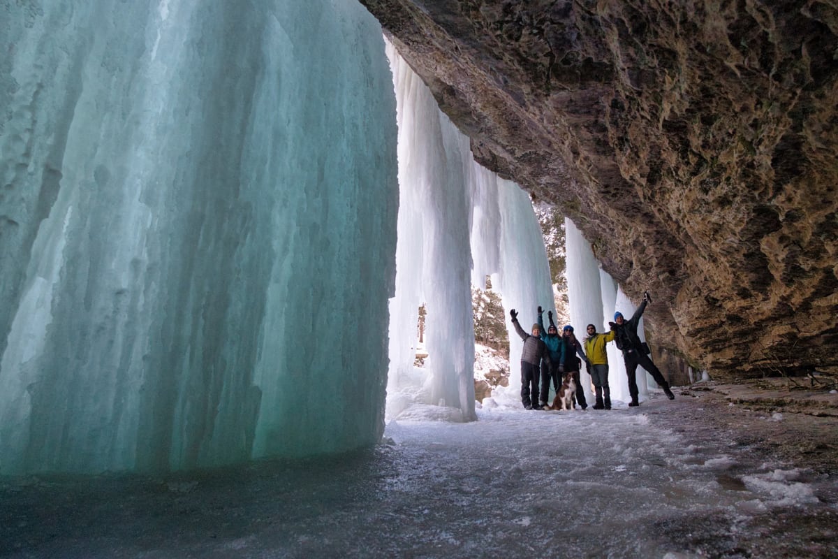 Group of hikers under a frozen waterfall.
