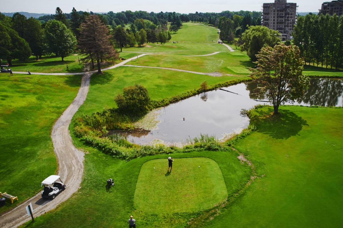 Aerial view of a golf course with a pond, a path and a golf cart.