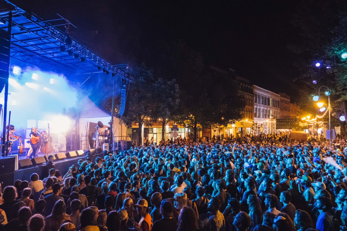 A crowd gathers in the evening in front of an outdoor stage at the Sherblues Festival.