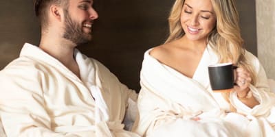 Couple relaxant au lit en peignoirs avec une tasse de café.