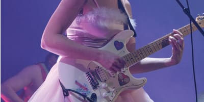 CEM - Une femme vêtue d'une robe rose chante et joue de la guitare électrique