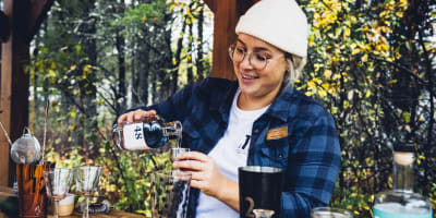 Distillerie du Fjord - Une femme prépare un breuvage alcoolisé, nature en arrière-plan.