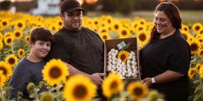 Famille de producteurs tenant de l'ail dans un champ de tournesols.