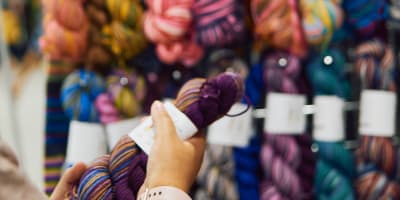 Festival de la fibre Twist - Une personne tient un écheveau de laine devant un présentoir
