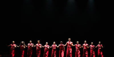 Festival des Arts de Saint-Sauveur - Des danseurs habillés en rouge sont disposés en ligne sur une scène noire