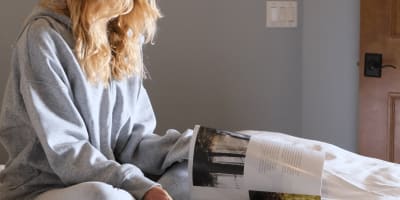 Une jeune femme assise sur le lit regardant un magazine avec son café.