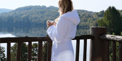 Une jeune femme en robe de chambre buvant son café sur le balcon.
