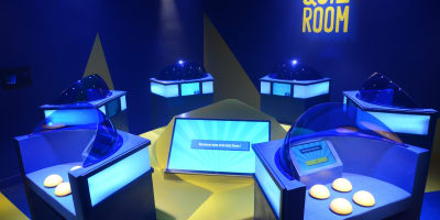 La Boîte à Questions – Quiz Room Montréal - Salle de jeux illuminée avec avec des stations individuelles équipées d'un écrans et boutons.