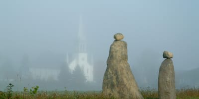 Les Amis du Patrimoine de Saint-Venant-de-Paquette - Two stone sculptures, with a church in the background