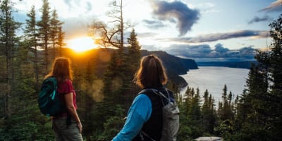 Parc national du Fjord-du-Saguenay - Two women on top of a mountain, forest and sunset in the background.