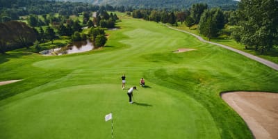 Trois personnes sur un vert au Golf Château-Bromont, avec la montagne en arrière-plan.