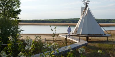 Femme marchant en peignoir marchant à côté d'un tipi sur le bord d'un lac en été.