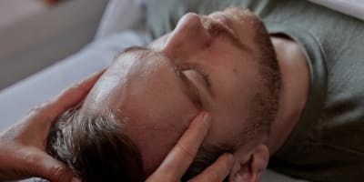 Un homme sur le dos se fait masser la tête.