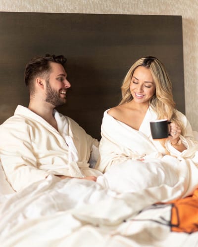 Couple relaxant au lit en peignoirs avec une tasse de café.