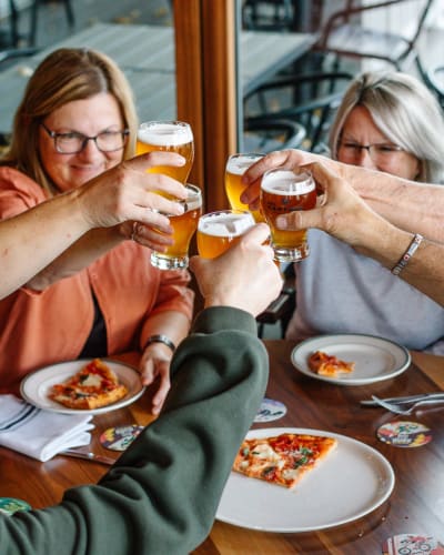 Des gens autour d'une table avec une pizza et de la bière de Des Cantons Microbrasserie.