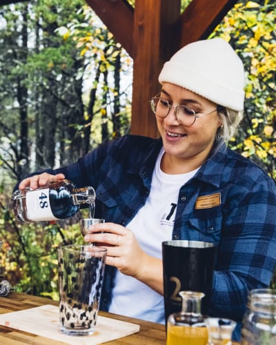 Distillerie du Fjord - Une femme prépare un breuvage alcoolisé, nature en arrière-plan.