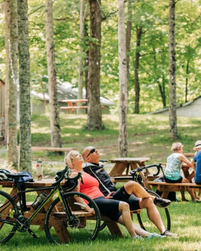 Érablière du Village - A man and a woman are seated at a picnic table, with their bikes leaning against it.