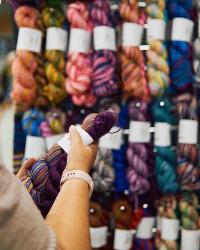 Festival de la fibre Twist - Une personne tient un écheveau de laine devant un présentoir