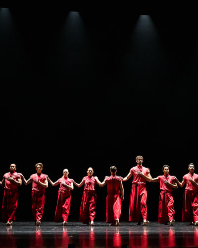 Festival des Arts de Saint-Sauveur - Des danseurs habillés en rouge sont disposés en ligne sur une scène noire