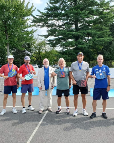 Jeux FADOQ provinciaux - On a pickleball court, there are six men wearing gold medals around their necks, and one man is dressed in a suit.