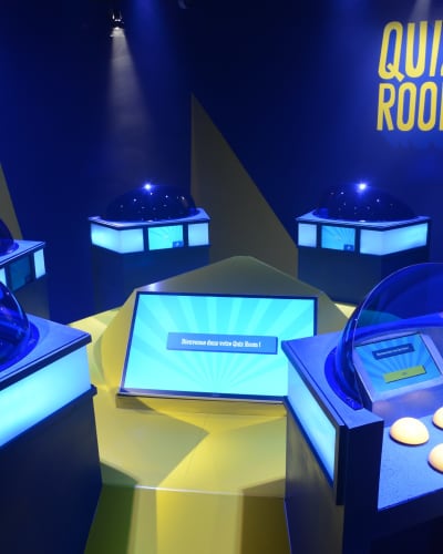 La Boîte à Questions – Quiz Room Montréal - Salle de jeux illuminée avec avec des stations individuelles équipées d'un écrans et boutons.