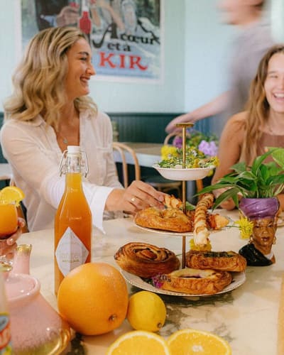 La Midinette - Women sitting at a table filled with pastries and fruit